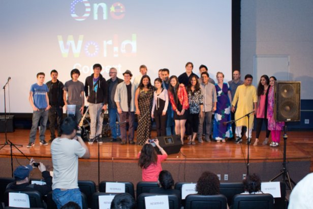 a group of students in various international clothing on a stage with the words "One World Concert" behind them